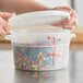 A hand holding a Choice translucent plastic food storage container with an open lid.