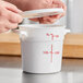 A person measuring out a Choice white round food storage container with a white measuring cup.