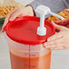 A person holding a container with a red lid pouring a red sauce.
