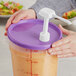A person holding a purple Choice pump dispenser lid over a container of liquid.