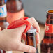 A person using a Franmara red plastic knuckle bottle opener to open a bottle of beer.
