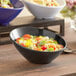 An Acopa black melamine bowl filled with salad, tomatoes, and basil.