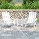 Two white Flash Furniture Adirondack chairs and a table on a stone patio.