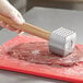 A person using a Choice aluminum meat tenderizer with a wood handle on a meat tenderloin.