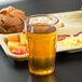 A Cambro Newport clear plastic tumbler filled with orange juice with a straw on a tray of food.