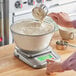 A person weighing flour in a bowl on an AvaWeigh digital scale.