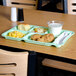 A green Carlisle 6 compartment tray holding chicken nuggets and a glass of milk on a table.