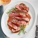A white plate with a Rastelli's Black Angus New York Strip Steak with sauce and rosemary.