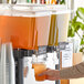 A person pouring Tractor Beverage Co. organic mandarin & cardamom concentrate into a juice dispenser.