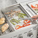 A person using a Backyard Pro Vegetable / Fish Tray to grill vegetables and meat.
