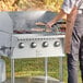 A man using a Backyard Pro stainless steel front shelf to cook meat on a grill.
