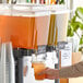 A person pouring Tractor Beverage Co. Organic Mandarin & Cardamom concentrate into a juice dispenser.