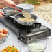A person cooking eggs in a pan on a Choice portable butane stove.