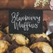 A brown table with blueberry muffins and a chalk card that says "blueberry muffins" on it.