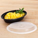 A black Pactiv Newspring VERSAtainer oval microwavable container with corn and parsley on a table.