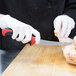 A person in white gloves using a Mercer Millennia Colors curved stiff boning knife to cut a piece of meat from a chicken.