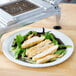 A plate of salad with sliced chicken on it under a Nemco Easy Chicken Slicer.