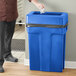 A man standing next to a Toter blue trash can with a blue lid.