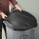 A man in a chef's jacket placing a black Toter lid on a trash can.