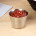 An American Metalcraft stainless steel sauce cup filled with ketchup on a table with a napkin.