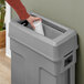 A hand using a Toter dark cool gray swing lid to put a white container in a trash can.
