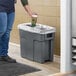 A person putting a coffee cup into a dark cool gray Toter Slimline trash can.