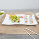A white American Metalcraft wavy stoneware platter with sushi rolls on a table.