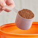 A hand using a 60 cc polypropylene scoop to pour brown granules into a container.