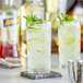 Two Acopa Zion beverage glasses filled with mint and lime juice on a bar counter.