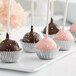 A chocolate covered cake pop in a silver foil mini baking cup on a white plate.