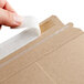 A person using a piece of tape to seal a Lavex Stayflats Kraft mailer box.