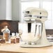 A KitchenAid almond cream tilt head countertop mixer with a bowl of cookies on a counter.