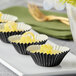 A row of Enjay black foil mini baking cups on a white plate filled with lemon curd cupcakes.