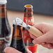 A hand holding the Franmara bottle opener with a beechwood handle opening a metal cap on a bottle.