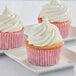 Three Enjay pink fluted baking cups with white polka dots holding cupcakes with white frosting.