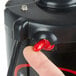 A finger pressing a red button on a black Bar Maid glass washer.