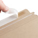 A hand seals a brown Lavex Stayflats rigid mailer with tape.