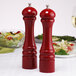Two Chef Specialties candy apple red pepper mills on a table with wine glasses.