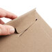 A hand opening a Lavex Stayflats kraft brown envelope with a piece of cardboard inside using a paper clip.
