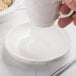A hand holding a CAC ivory scalloped edge demitasse saucer over a bowl of food.
