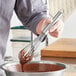 A person using a Choice stainless steel French whisk to mix chocolate in a bowl.