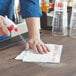 A person spraying a Dixie white and red striped foodservice towel on a table.