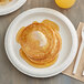 A stack of pancakes with butter on a Dixie white paper plate with a fork and knife.