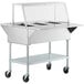 A silver ServIt electric steam table with clear sneeze guard on wheels.