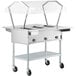 A ServIt stainless steel electric steam table with a clear sneeze guard over hot food on wheels.