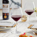A table with Acopa burgundy wine glasses and a glass of red wine on it.