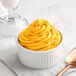 A white ramekin filled with yellow Creamery Ave. mango soft serve mix with a spoon.