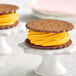 Two ice cream sandwiches on white pedestals with yellow frosting on top.