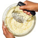 A hand using an OXO black masher to make mashed potatoes.