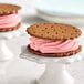 Two cookies with pink ice cream in the middle on a white surface.